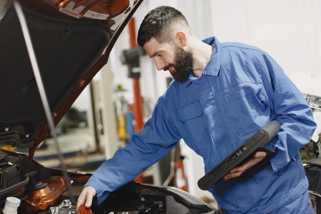 man in blue overalls checking on a vehicle engine